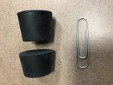 A close up view of two rubber stoppers sitting beside a paper clip